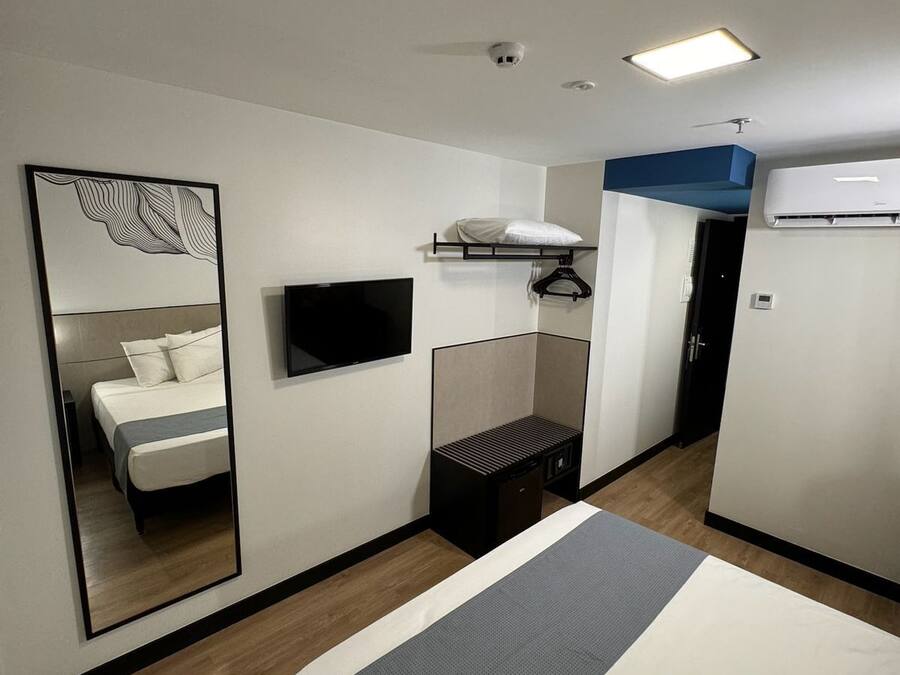 Habitación de hotel moderna con cama, televisor de pantalla plana, espejo, armario y unidad de aire acondicionado.