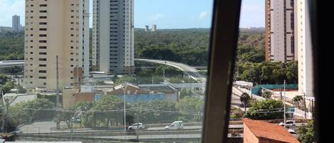 Vista a través de una ventana que muestra un paisaje urbano con edificios altos, una autopista y algo de vegetación.