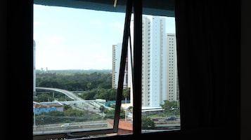 Vista a través de una ventana con un rascacielos, un puente y vegetación al fondo.