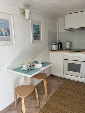 Eine kleine Küche mit einer weißen Arbeitsplatte, zwei Barhocker, einem Toaster, einem Wasserkocher und einem gerahmten Bild an der Wand.