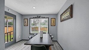 A conference room with a long table, chairs, a window with blinds, framed pictures on the wall, and a ceiling light.
