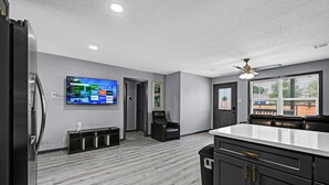 A modern kitchen with a large island, dark cabinetry, and a flat-screen TV mounted on the wall.