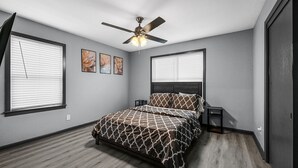 A bedroom with a bed, ceiling fan, two bedside tables, and artwork on the wall.