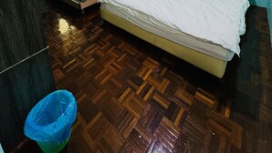 Habitación con dos camas, ventilador de techo, aire acondicionado, ventana con cortinas y piso de parquet de madera.