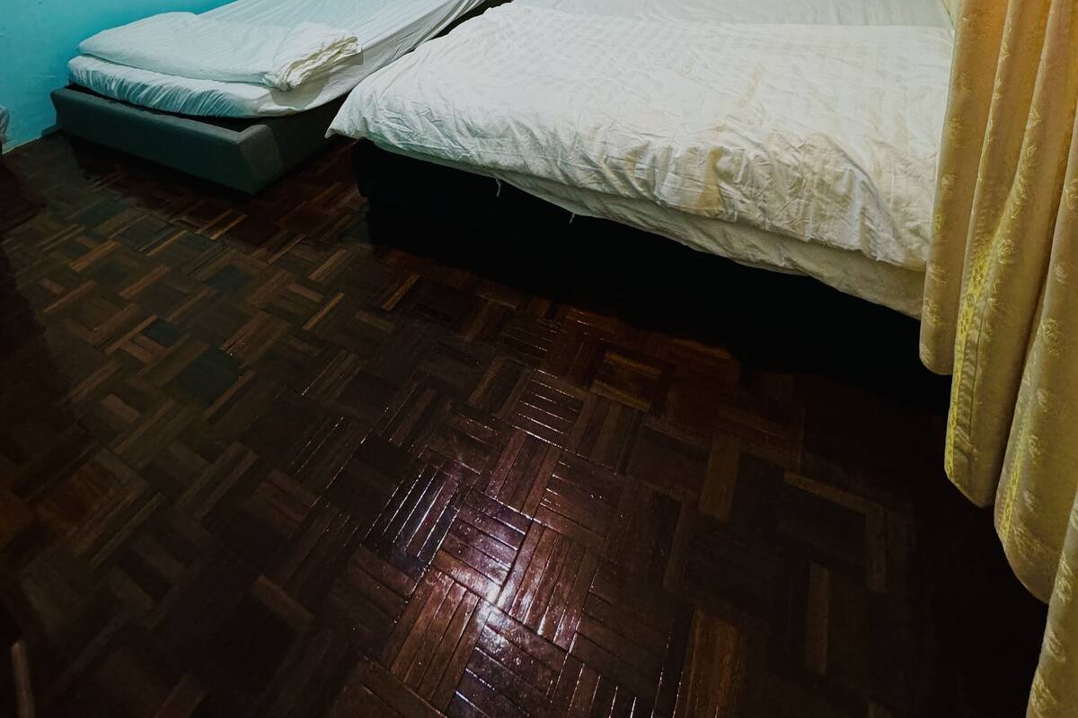 A room with two beds, wooden flooring, and an air conditioning unit on the wall.