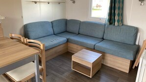 Un salon moderne avec un canapé d’angle, une table basse en bois et un coin repas comprenant une table et des chaises en bois.