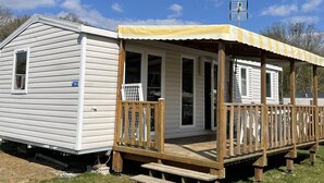 Une maison mobile dotée d’un porche et d’une petite terrasse, avec une antenne métallique et une plaque d’immatriculation.
