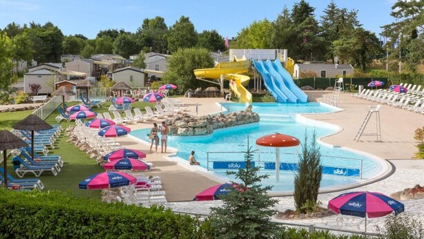 Un espace piscine équipé d’un toboggan, de chaises longues et de parasols.