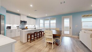Una cocina moderna con muebles blancos, una isla central con taburetes, una mesa de comedor con sillas y grandes ventanales que ofrecen vistas.
