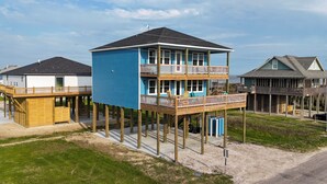 Una casa frente al mar de varios pisos con terraza de madera, balcón y porche cubierto.