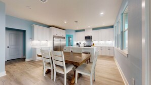 Una cocina moderna con armarios blancos, una isla central y un comedor con sillas blancas.