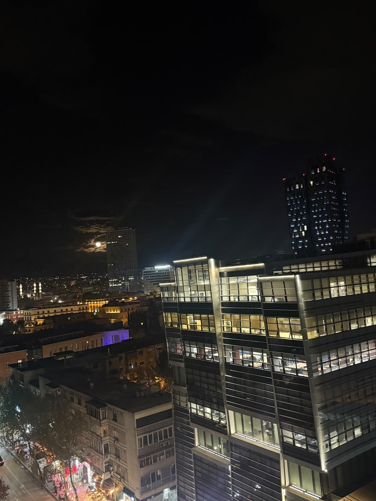A nighttime cityscape with modern buildings, including a multi-story structure with illuminated windows.