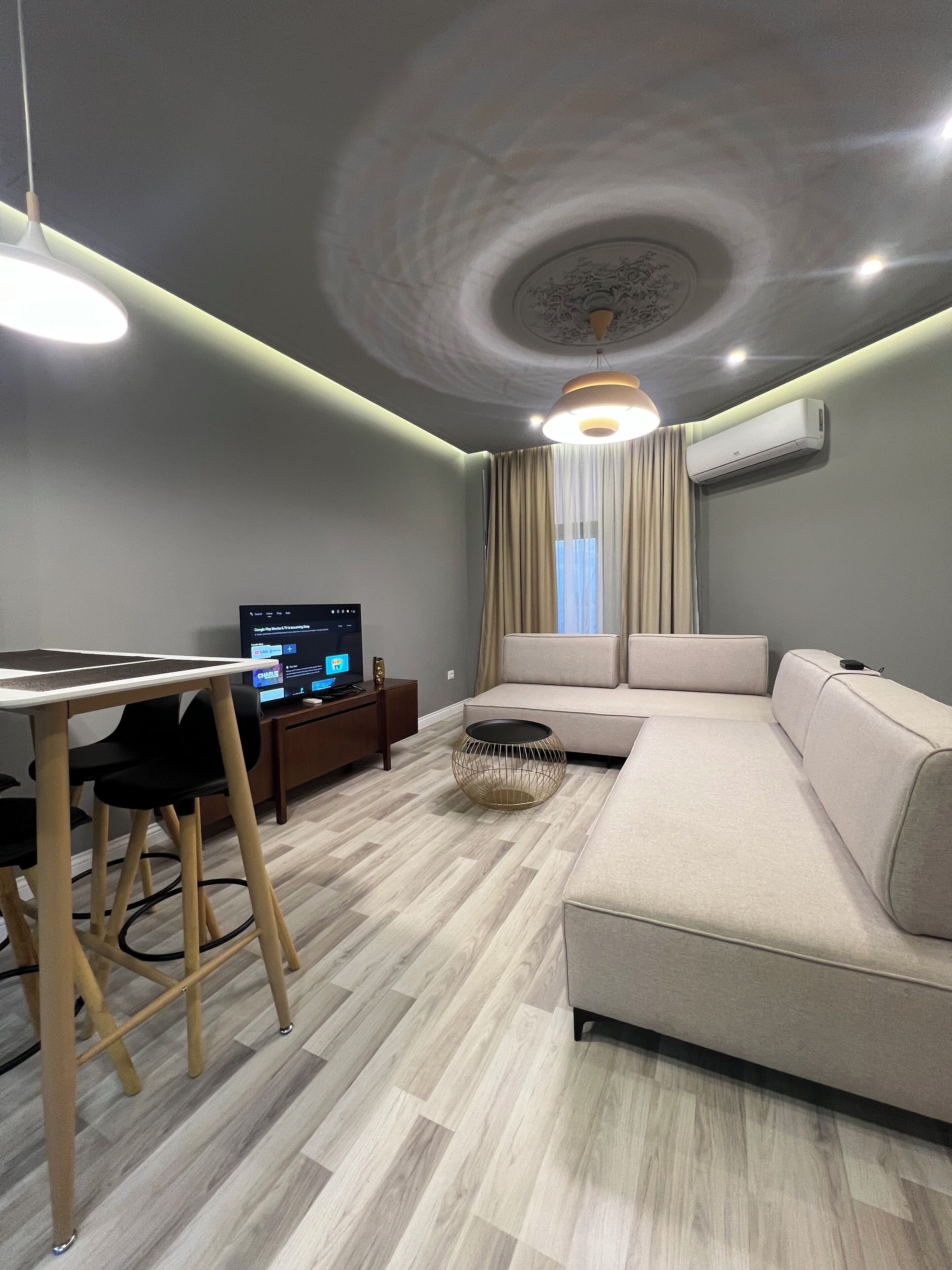 A modern living room with a sofa, a dining table with chairs, a TV, and an air conditioning unit.
