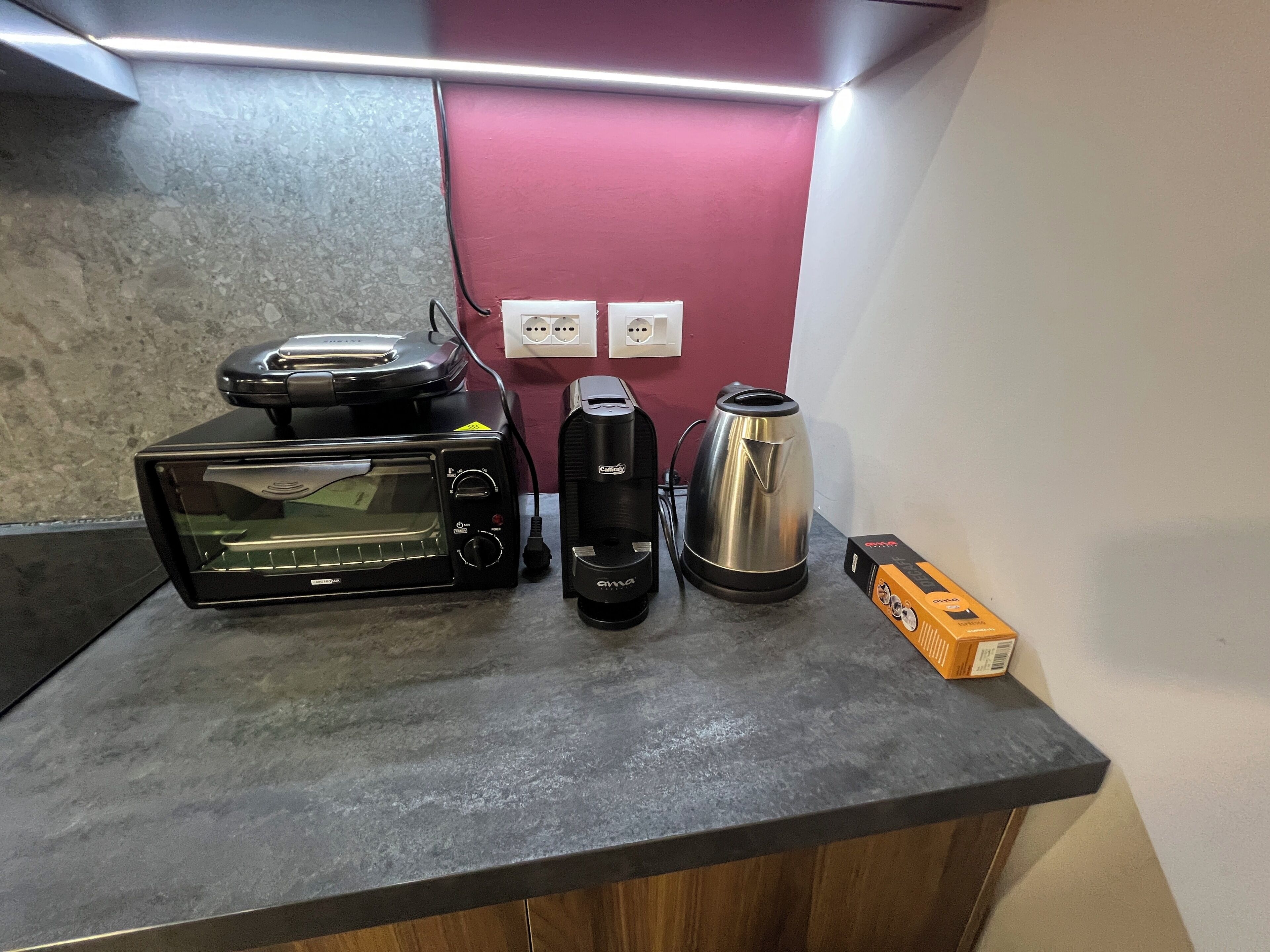 A kitchen counter with a toaster oven, a coffee maker, a kettle, and a box.