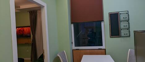 Una habitación pequeña y bien iluminada con una mesa de comedor y dos sillas, una ventana con persiana, y una puerta que da a otra habitación.