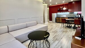 A modern living room with a sectional sofa, a round coffee table, and a dining area with a red accent wall.