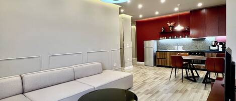 A modern living room with a sectional sofa, a round coffee table, and a dining area with a red accent wall.