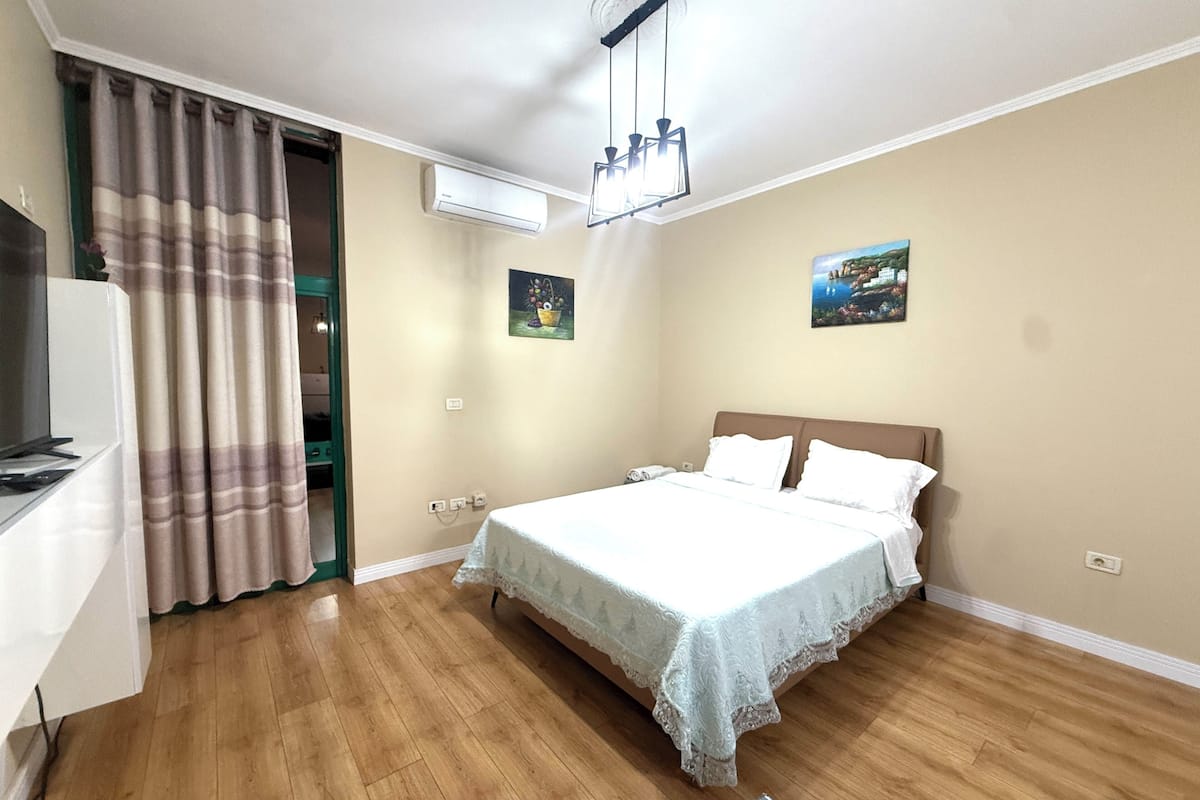 Een slaapkamer met een bed, gordijnen, een airconditioning, een schilderij en een televisie.