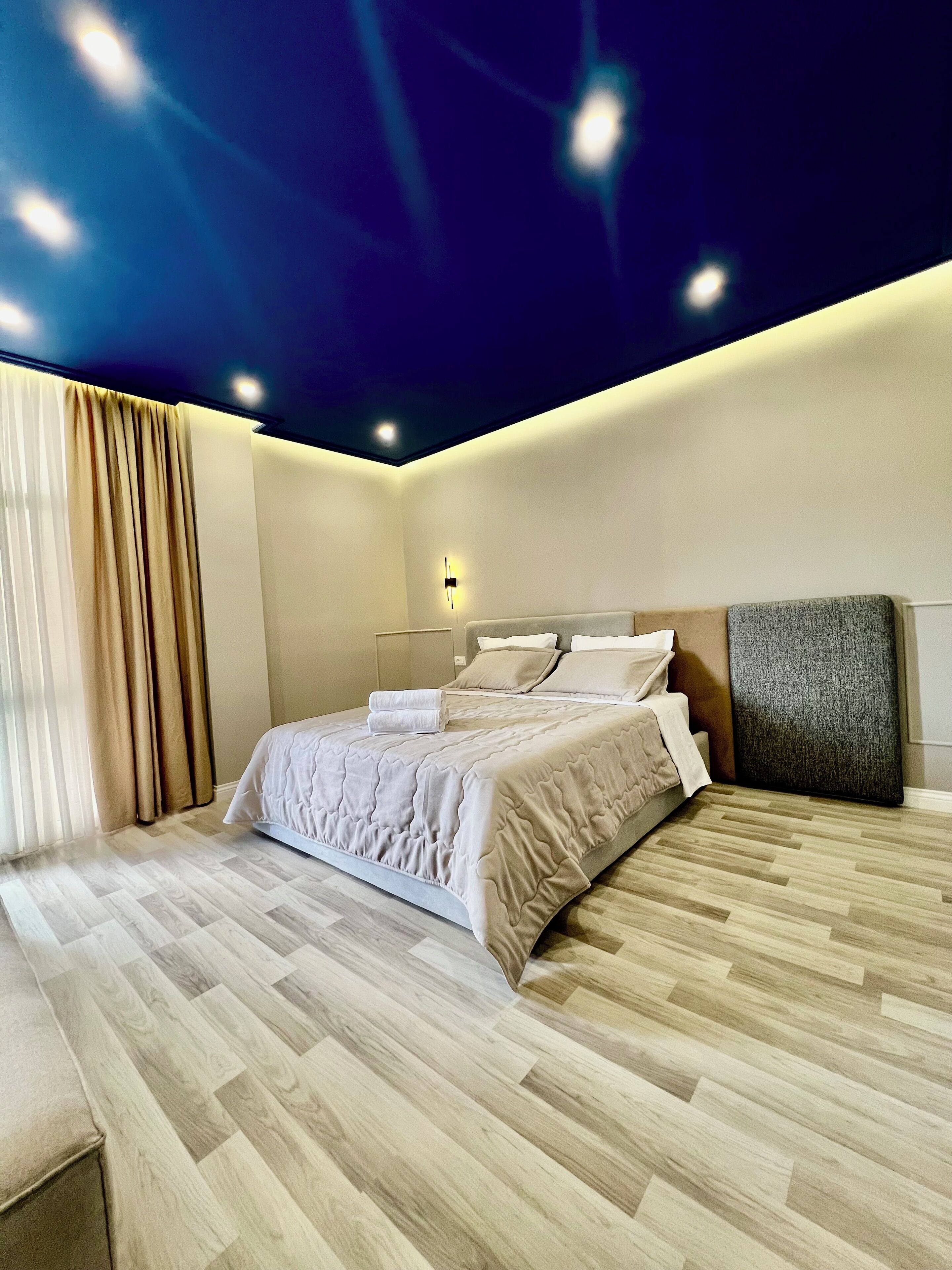 A modern bedroom with a large bed, wooden flooring, and a ceiling with recessed lighting.