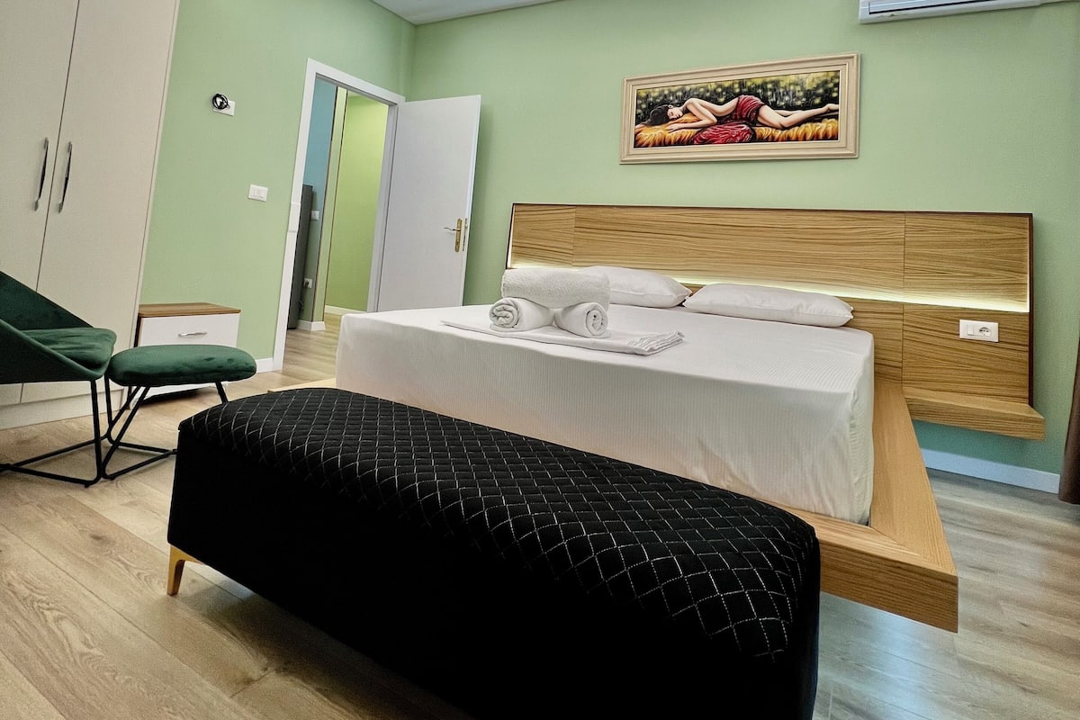 Een moderne slaapkamer met een bed, een groene fauteuil, een kledingkast en een plafondlamp.
