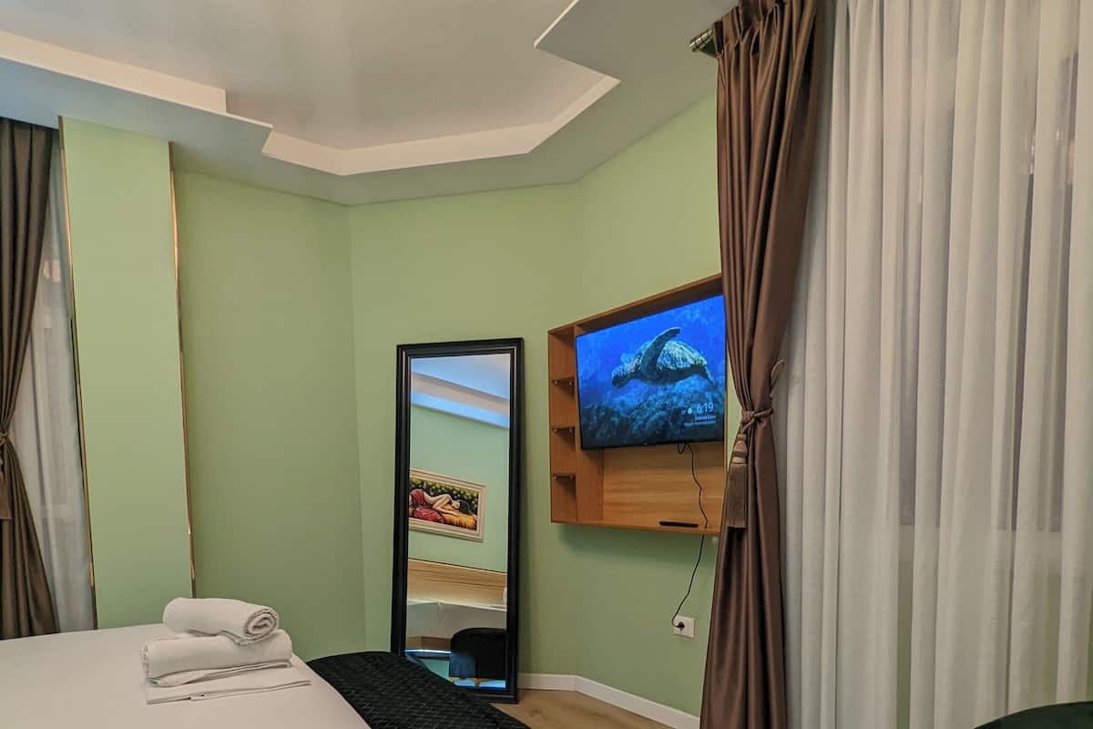 Een hotelkamer met een bed, een kleine bank, een aan de muur bevestigde televisie en een spiegel.