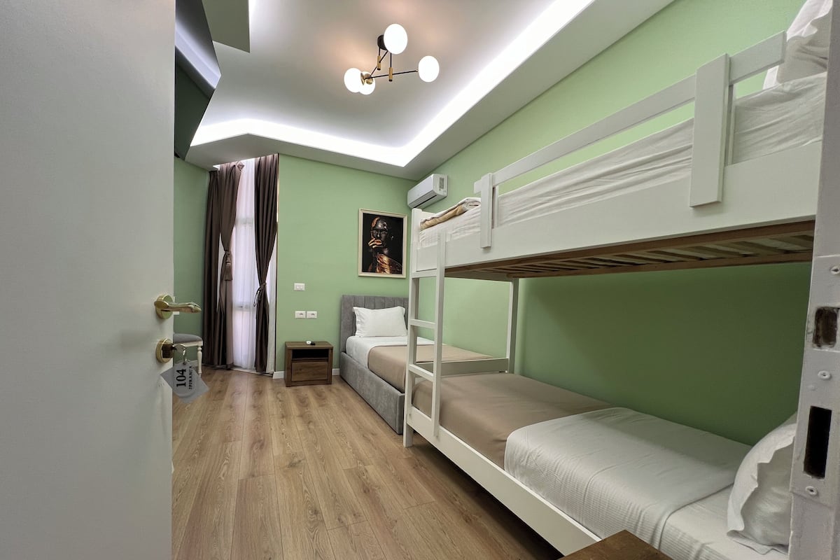 Een kamer met stapelbedden, een klein nachtkastje, een wandairconditioner en een plafondlamp.