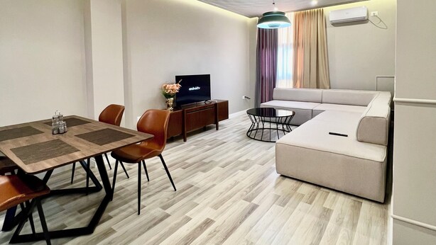 A modern living room with a dining area, a sofa, a TV, and a ceiling light fixture.