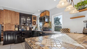 A modern kitchen with dark wooden cabinets, a large island with a mosaic tile top, and a built-in oven. - Victorian 4BR/2BA Modern Home (Norwich)