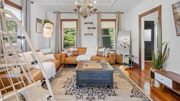 A spacious living room with a brown leather sofa, a wooden coffee table, and a chandelier. - Victorian 4BR/2BA Modern Home (Norwich)