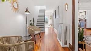 A hallway with a staircase, wicker furniture, and a radiator. - Victorian 4BR/2BA Modern Home (Norwich)