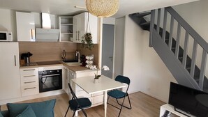 Una cocina funcional con electrodomésticos modernos, un comedor con mesa y sillas, y una escalera que sube a un nivel superior.