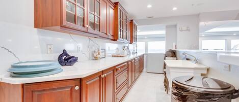 A modern kitchen with wooden cabinets, a white countertop, and a black trash bin.