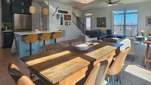 A modern kitchen with a central island, a dining area with a wooden table, and a staircase leading to a lofted living space.