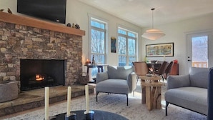 A living room with a stone fireplace, a flat-screen TV, and a dining area with a round table and chairs.