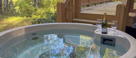 A hot tub with a wooden deck and a bottle of champagne.