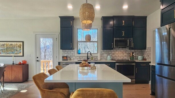 A modern kitchen with dark cabinets, a large island, and a hanging light fixture.