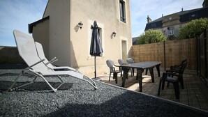 An outdoor patio with a table and chairs, a lounge chair, and a flag. - Villa Joséphine, Appt 2-4 Personnes, Bord de Mer, à Asnelles, à 300m de la Plage (Asnelles)