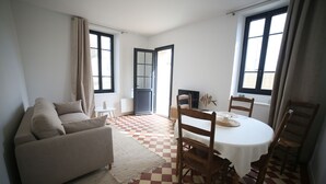 A living room with a checkered floor, a sofa, a dining table with chairs, and large windows. - Villa Joséphine, Appt 2-4 Personnes, Bord de Mer, à Asnelles, à 300m de la Plage (Asnelles)
