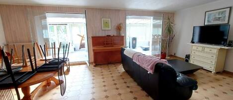 A spacious living area with a sofa, a dining table with chairs, a TV, and a cabinet.