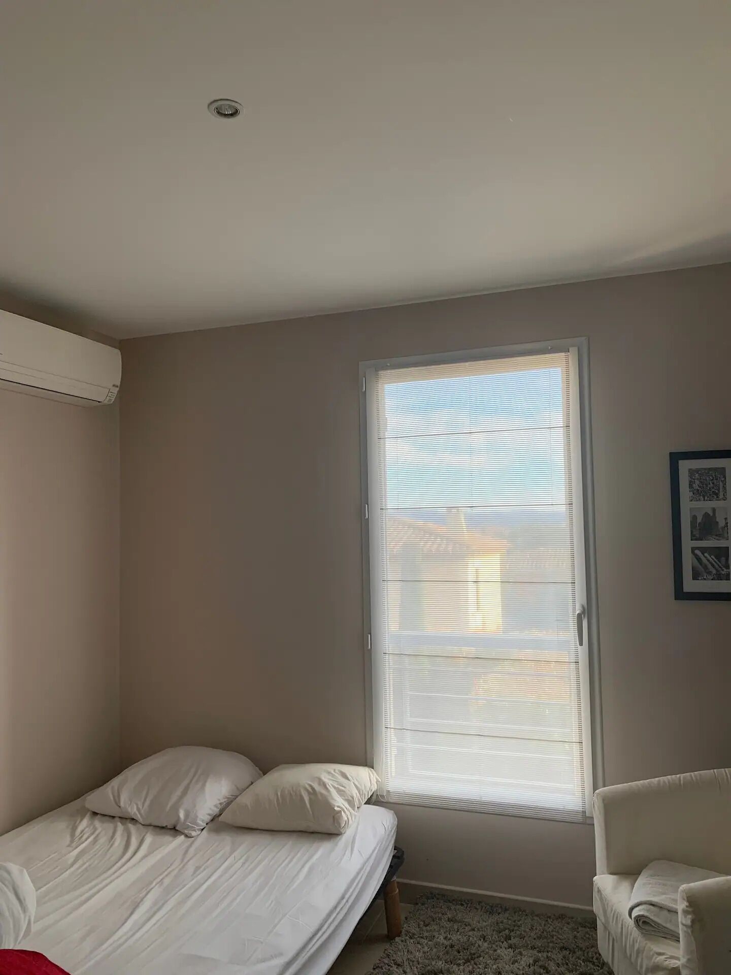 A bedroom with a single bed, a window with blinds, a chair, and a ceiling vent.