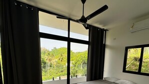 A bedroom with a bed, a ceiling fan, and a large window with curtains. - Romantic Spanish villa w/Infinity Pool — 10 min from the beach! (Las Terrenas)