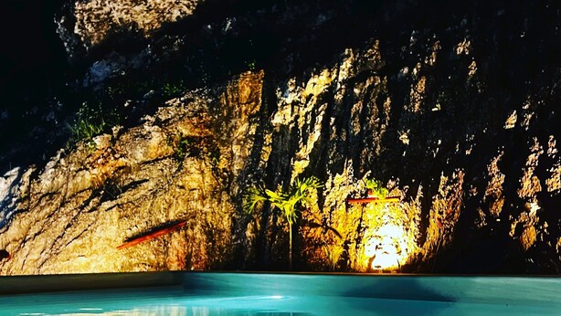 A swimming pool with clear blue water, surrounded by rocky cliffs and illuminated by artificial lighting. - Romantic Spanish villa w/Infinity Pool — 10 min from the beach! (Las Terrenas)