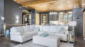 A modern living room with a sectional sofa, a coffee table, and a kitchen area in the background.
