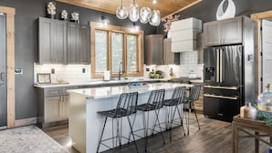 A modern kitchen with a large island, bar stools, stainless steel appliances, and wooden ceiling accents.
