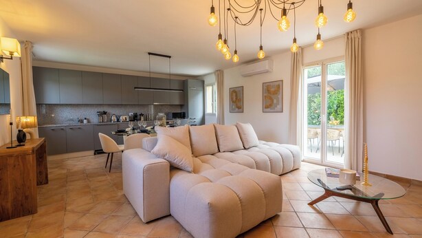 Ein modernes Wohnzimmer mit einem beigefarbenen Ecksofa, einem Glastisch und einem Essbereich mit Holztisch.