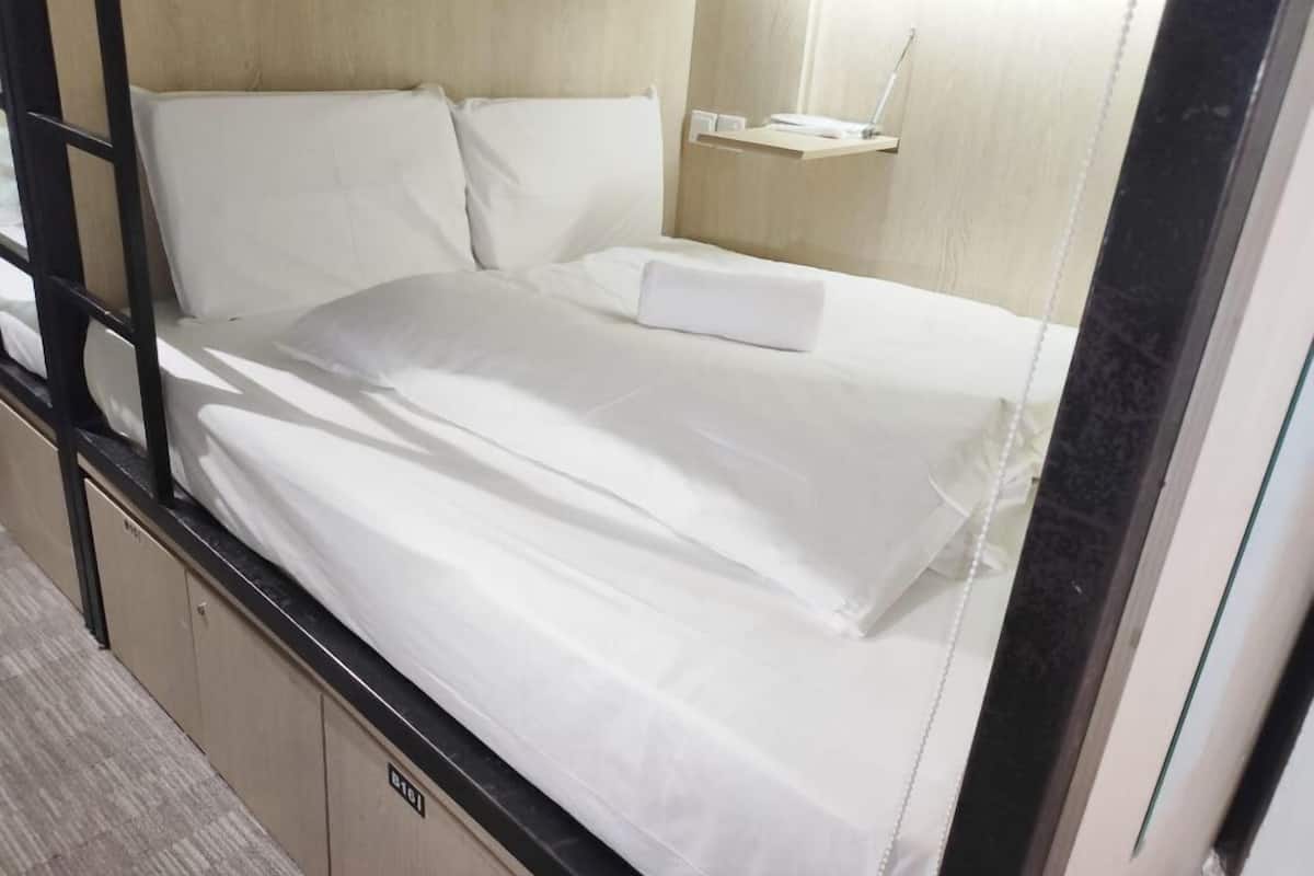 A bunk bed with white bedding, a bedside table with a lamp, and a small shelf.