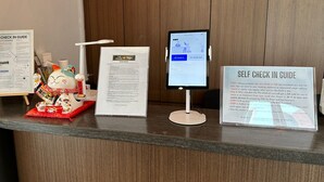 Un kiosque d’enregistrement automatisé, un guide d’enregistrement automatisé et une statue de chat décorative dans le hall d’accueil d’un hôtel.