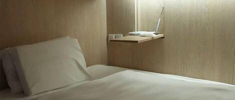 A neatly made bed with white linens, a bedside table with a lamp, and a wooden wall panel.