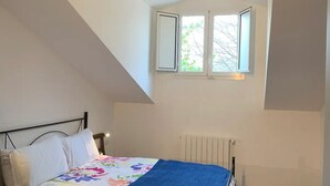 Ein Schlafzimmer mit Bett, Heizkörper, einem Fenster mit Blick auf Bäume und einer geneigten Decke.