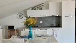 Eine moderne Küche mit weißen Schränken, ein Essbereich mit weißem Tisch und Stühlen sowie eine Vase mit gelben Blumen.